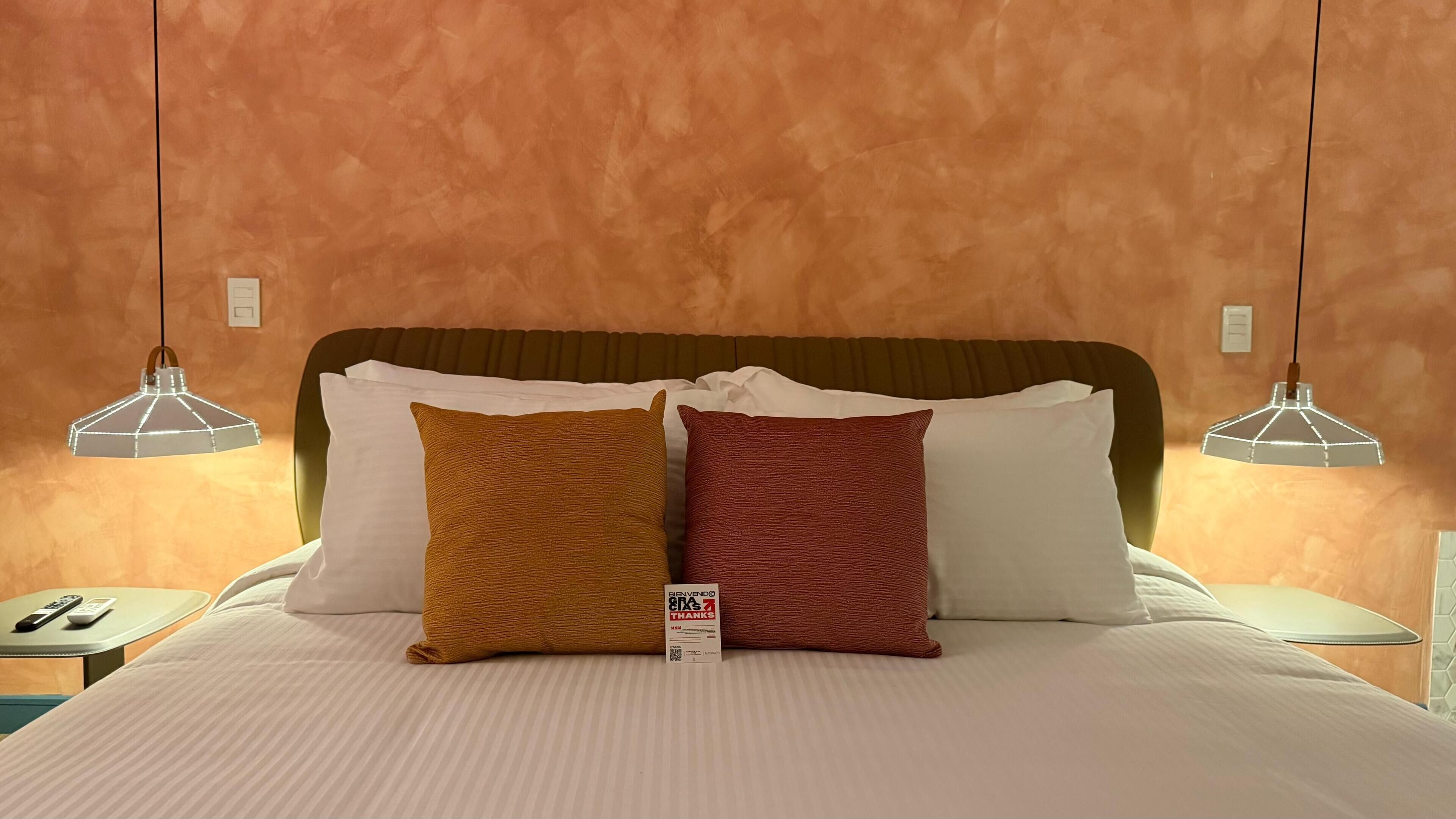 Een hotelkamer met een groot bed, twee nachtkastjes en twee hanglampen.