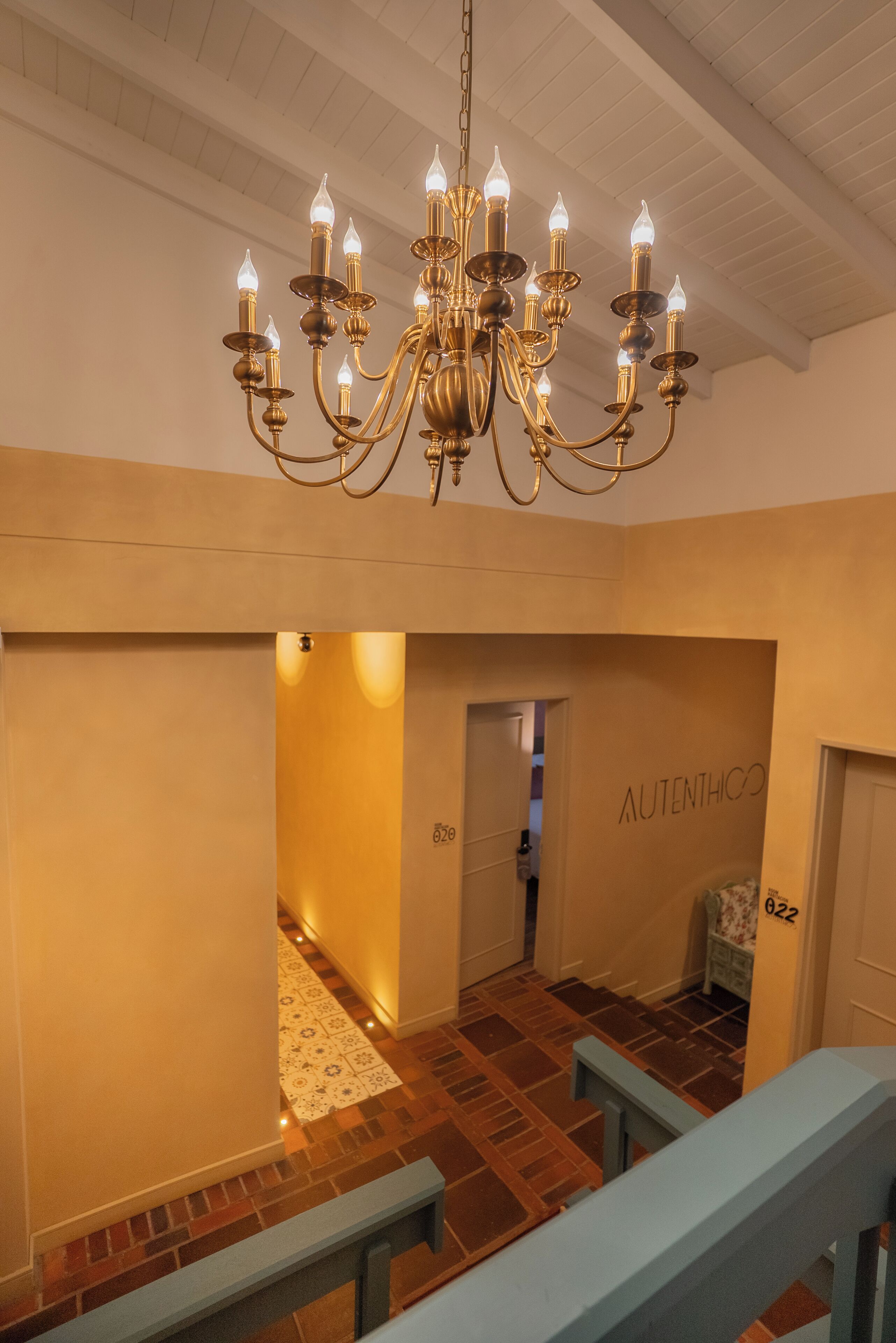 A chandelier in a hallway with a patterned floor and a door labeled "Authentico".