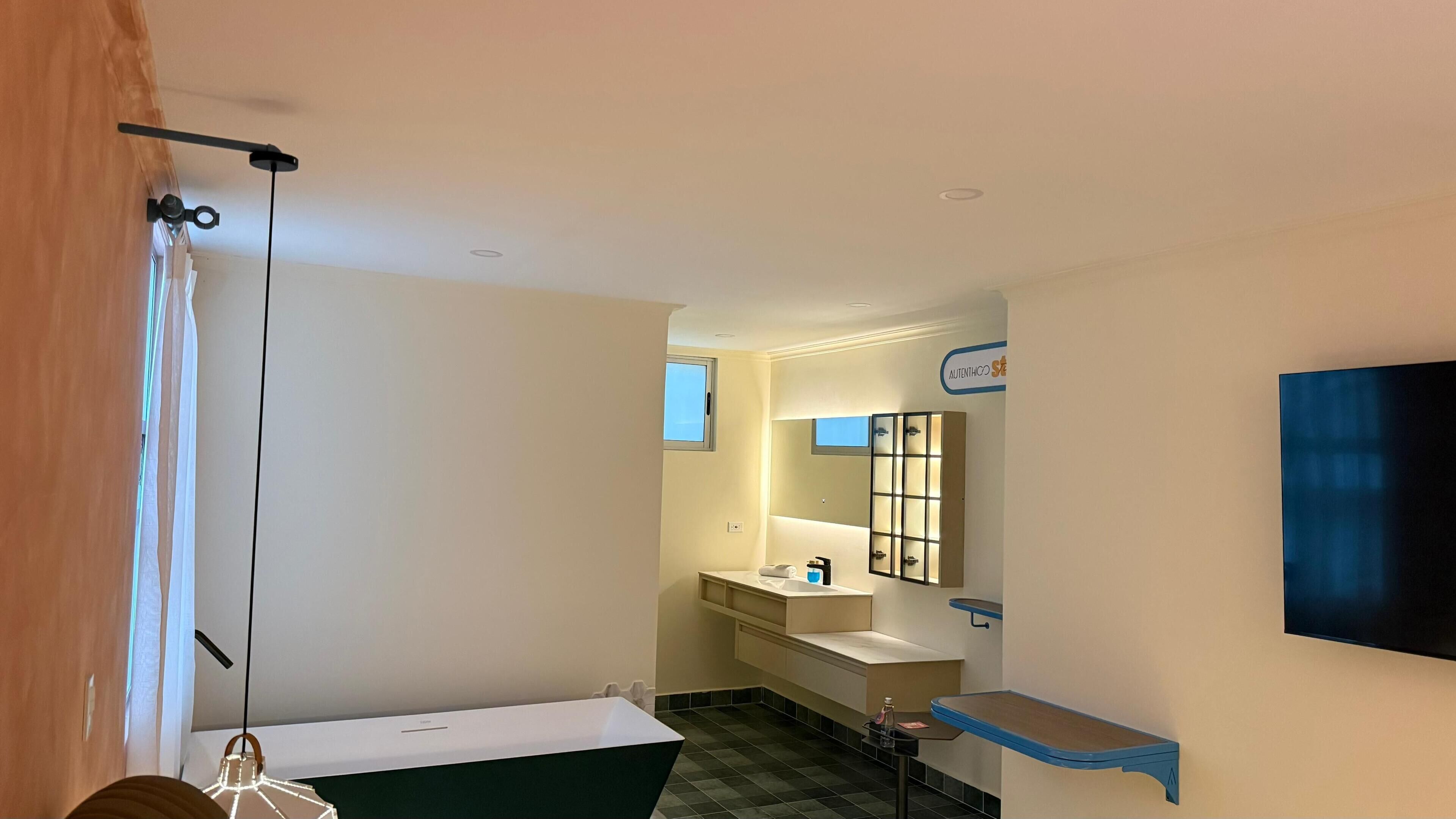 A hotel bathroom with a bathtub, a sink, a mirror, and a television mounted on the wall.