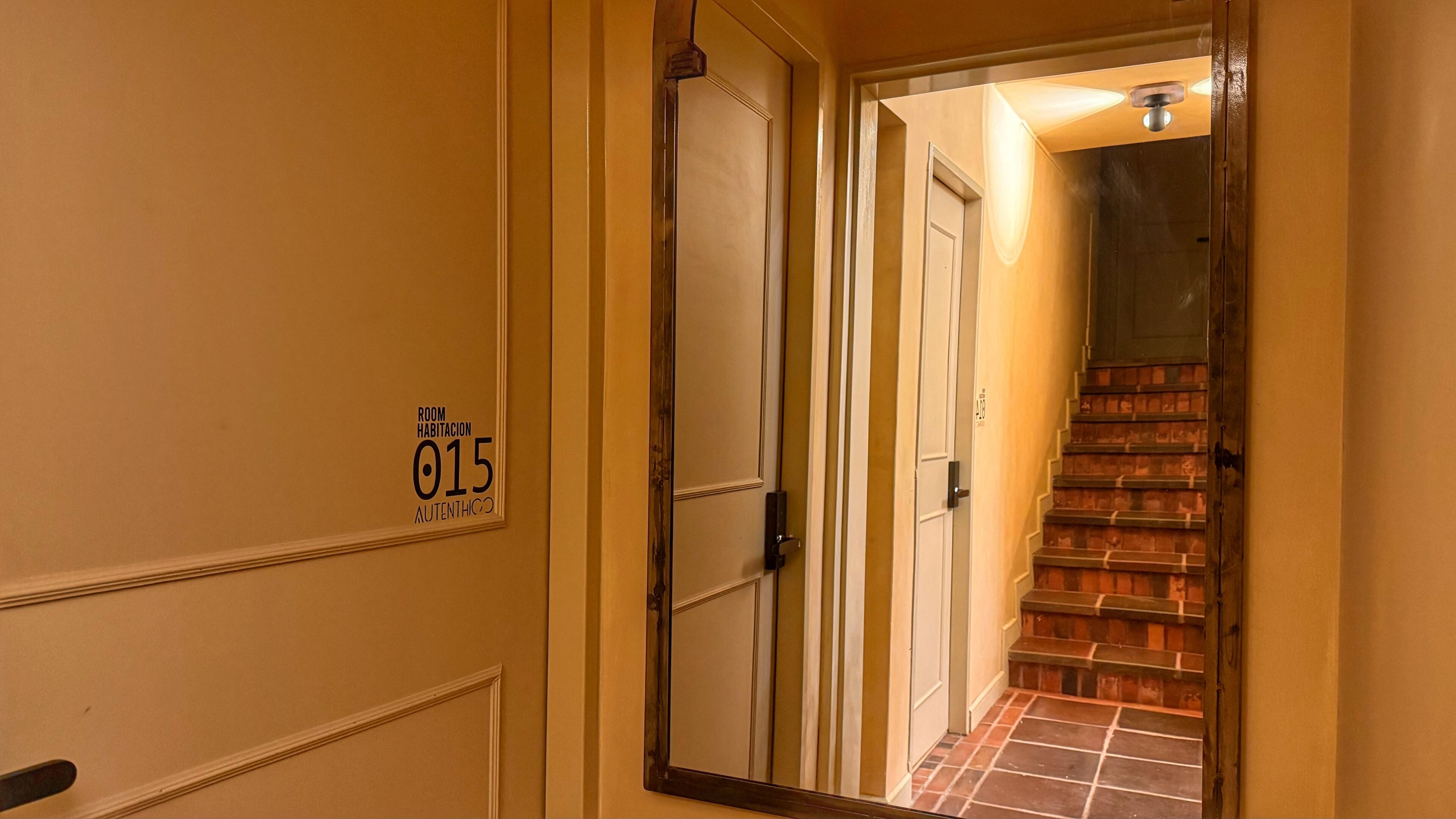 A hallway with a door labeled "ROOM HABITACION 015 AUTENTHICO" and a staircase leading to another room.