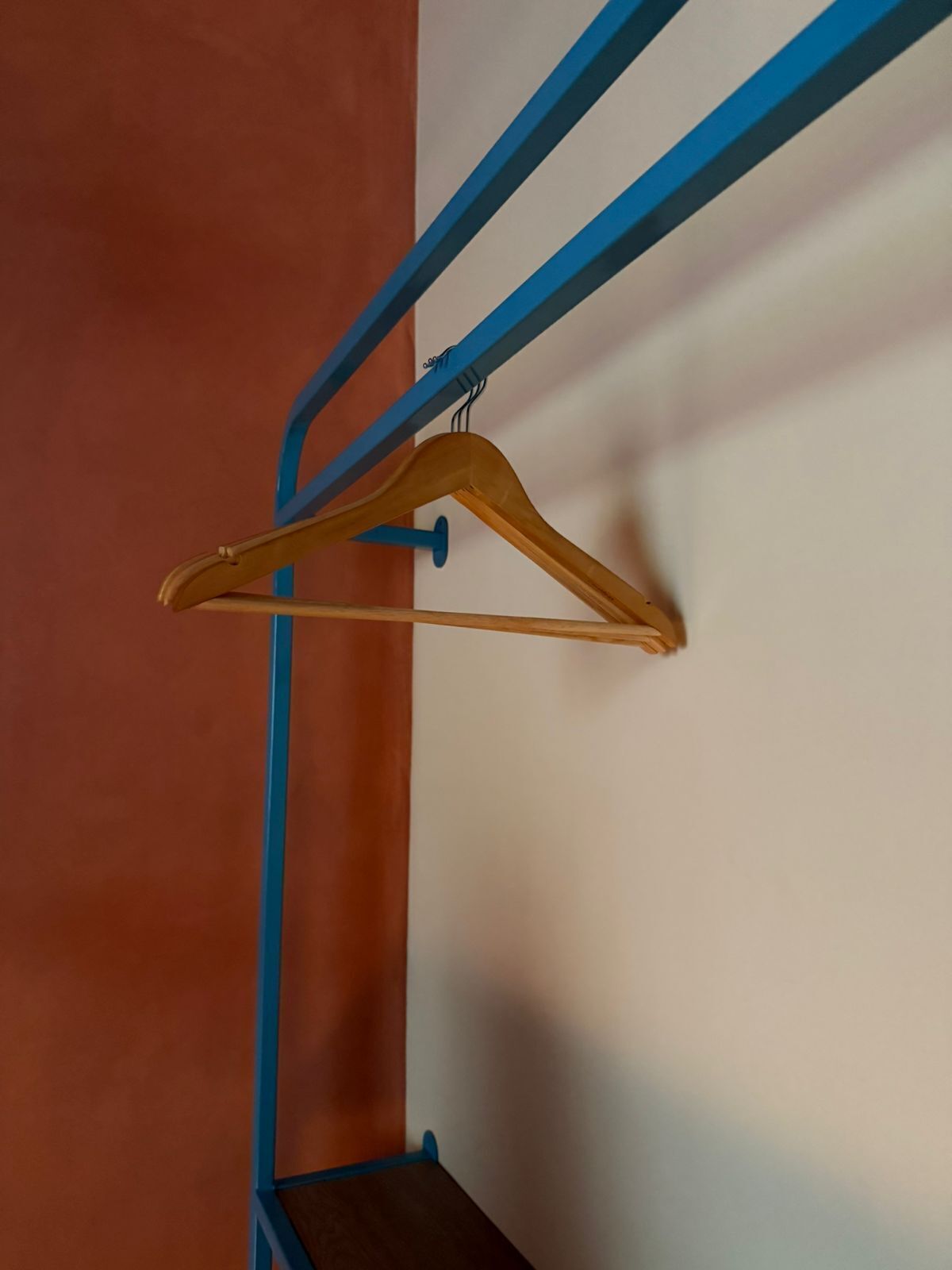 A corner of a room with a blue metal rack holding a wooden hanger.