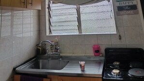 A kitchen with a sink, stove, wooden cabinets, and a window with a curtain.