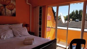 Une chambre d’hôtel avec un lit, une chaise et une grande fenêtre donnant sur le toit et les arbres.