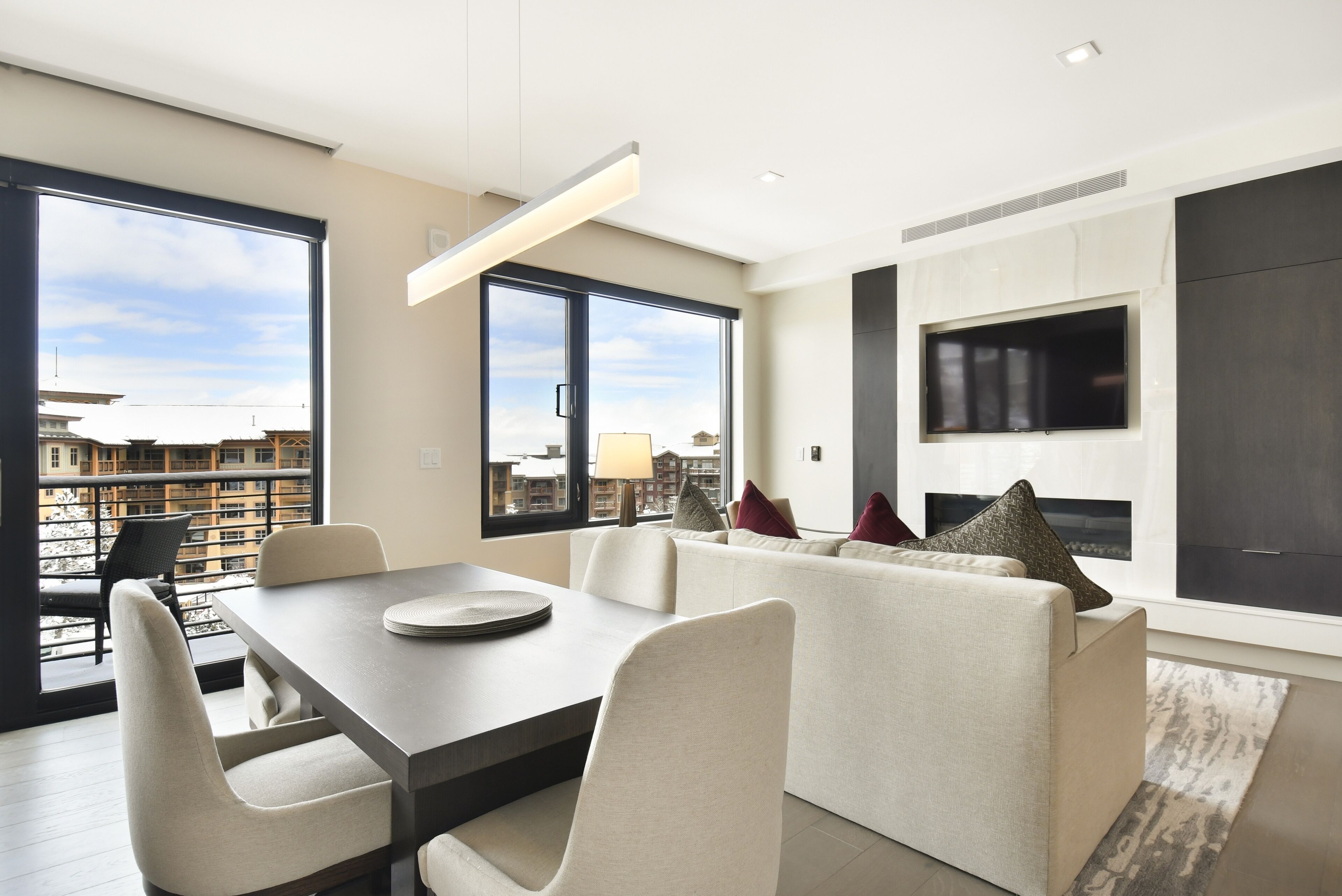 A modern living room with a dining area, large windows, and a flat-screen TV.