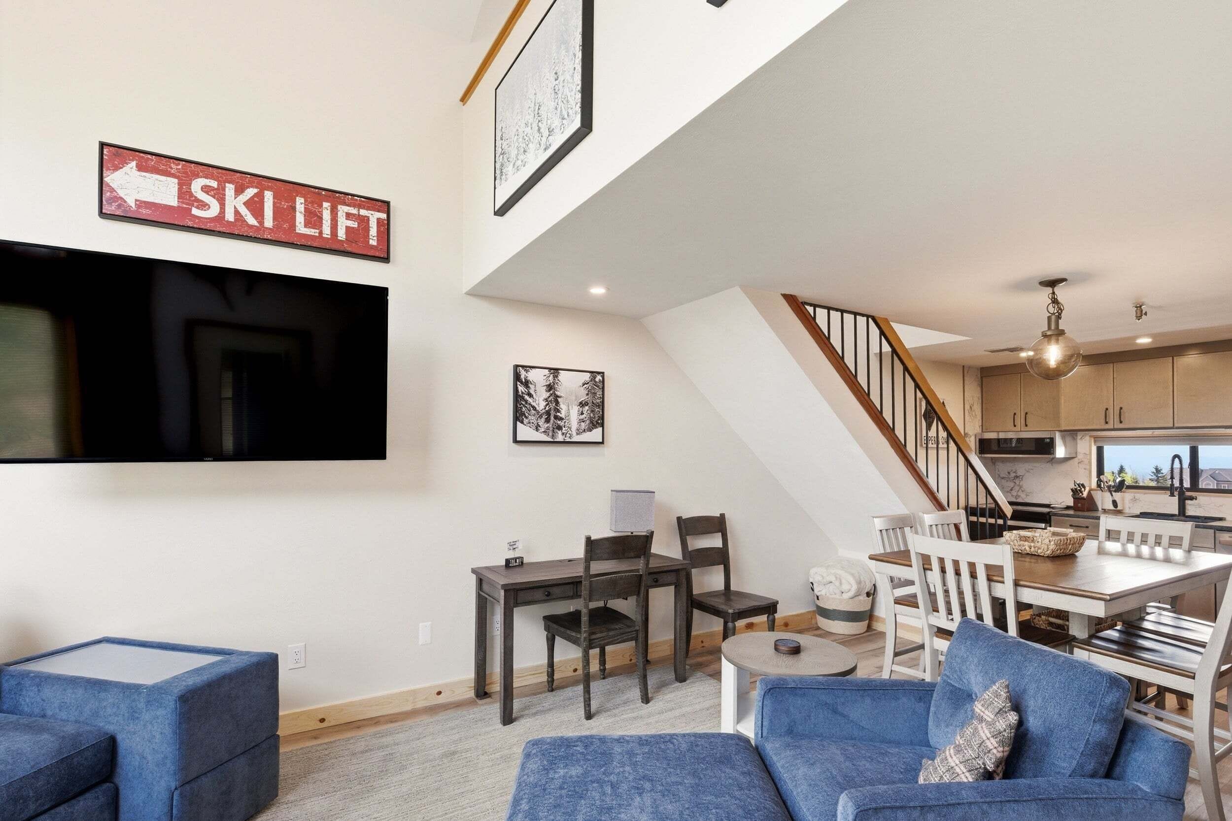 A modern living room with a ski lift sign, a flat-screen TV, and a dining area with a staircase.