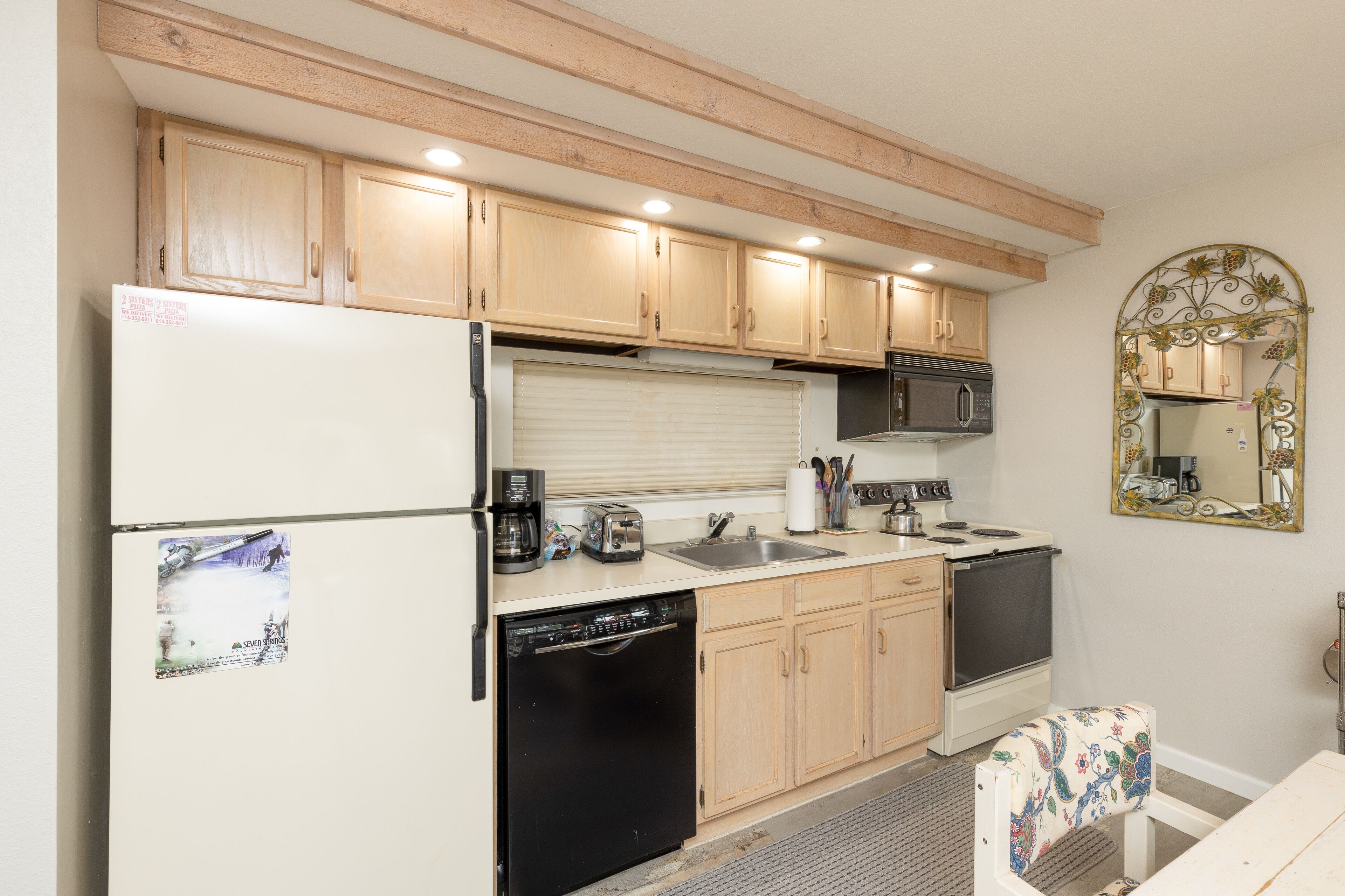 A compact kitchen with wooden cabinets, a refrigerator, a dishwasher, a stove, and a sink.