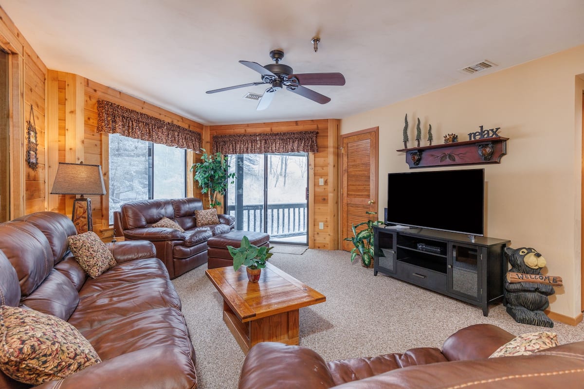 A cozy living room with a brown leather couch, a wooden coffee table, a TV stand, and a ceiling fan.