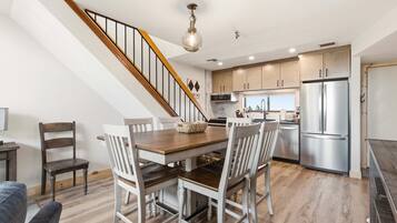 A modern kitchen with a wooden staircase, a dining table with chairs, and a stainless steel refrigerator.