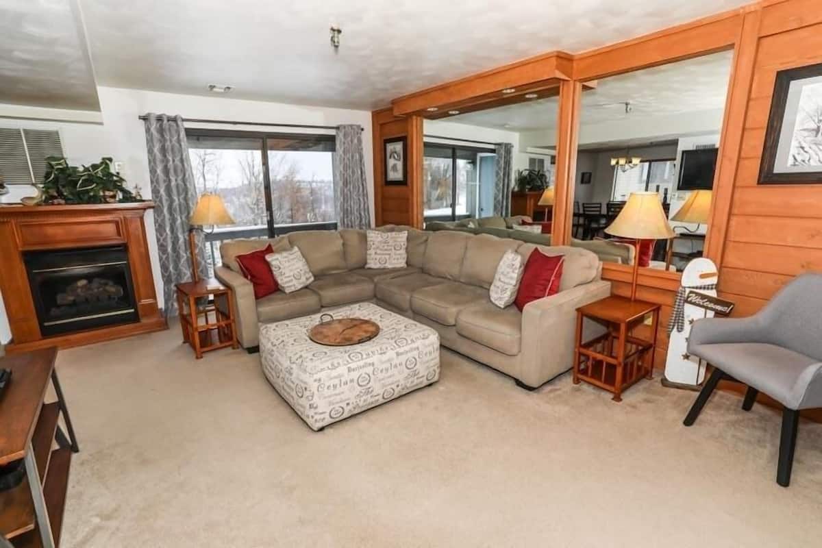 A cozy living room with a sectional sofa, a coffee table, a fireplace, and a large mirror.