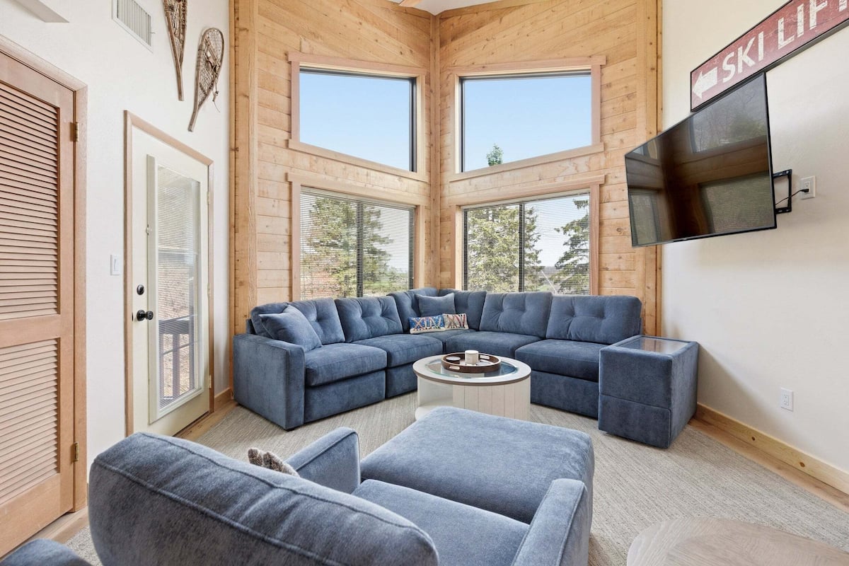 A modern interior with a sectional sofa, a flat-screen TV, and large windows.