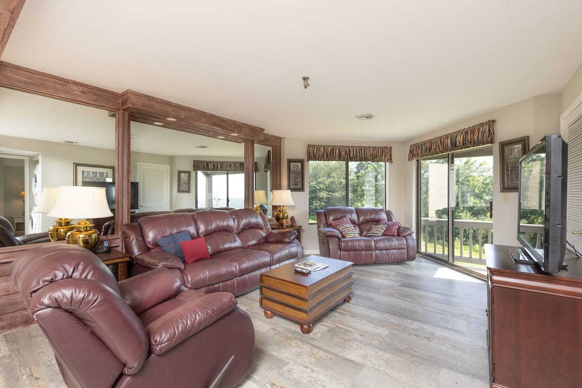 A spacious living room with leather sofas, a wooden coffee table, and a large mirror.