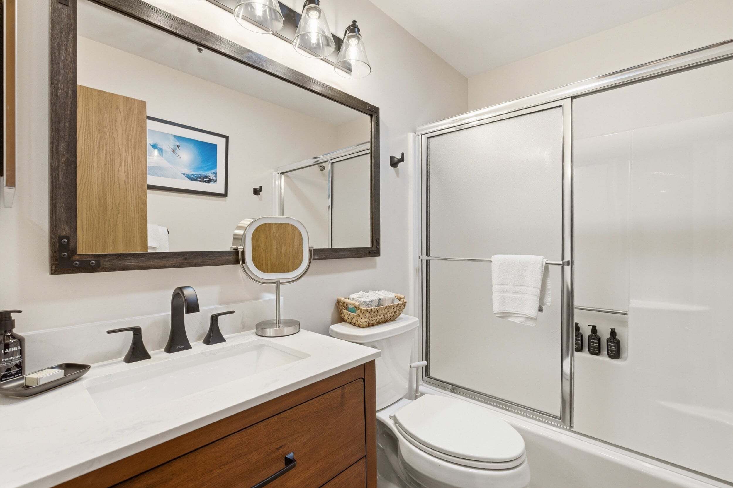 A bathroom with a white sink, a mirror, a toilet, and a shower.