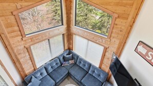 Habitació d'angle amb un sofà modular, dues finestres grans, un ventilador de sostre i una televisió.