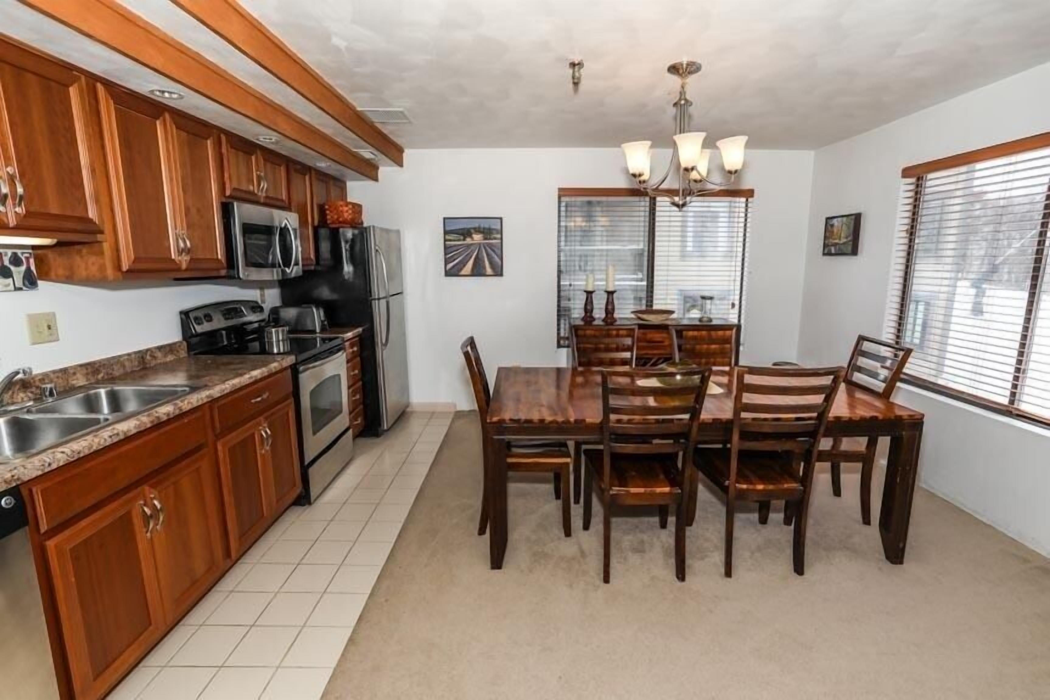 A kitchen with wooden cabinets, a microwave, a refrigerator, and a dining table with chairs.