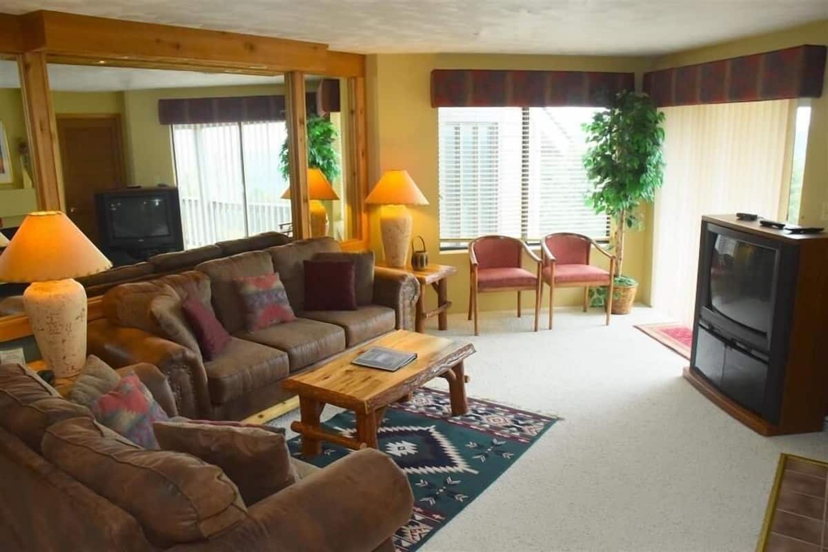 A living room with a brown sofa, a wooden coffee table, a TV, and a lamp.