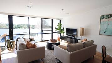 A modern living room with a sofa set, a television, and a large window offering a view of the outdoors.