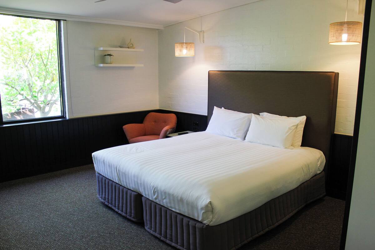 A hotel room with a large bed, a chair, a window, and a wall-mounted shelf.