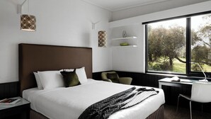 A modern hotel room with a large bed, a desk, and a view of trees through the window. - Waurn Ponds Estate (Waurn Ponds)