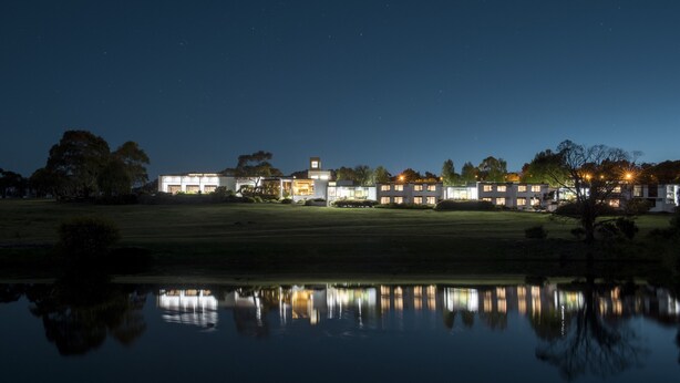 A nighttime view of a modern building complex with multiple illuminated windows, reflecting on a calm body of water. - Waurn Ponds Estate (Waurn Ponds)