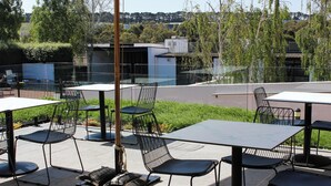 Un espace extérieur aménagé en terrasse, avec des tables et des chaises, offrant une vue sur le paysage urbain et un bâtiment moderne en arrière-plan.