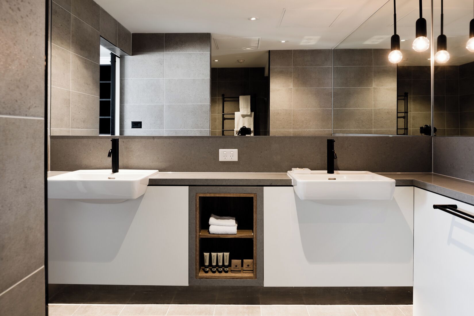 A modern bathroom with two sinks, a mirror, and a shelf with toiletries.