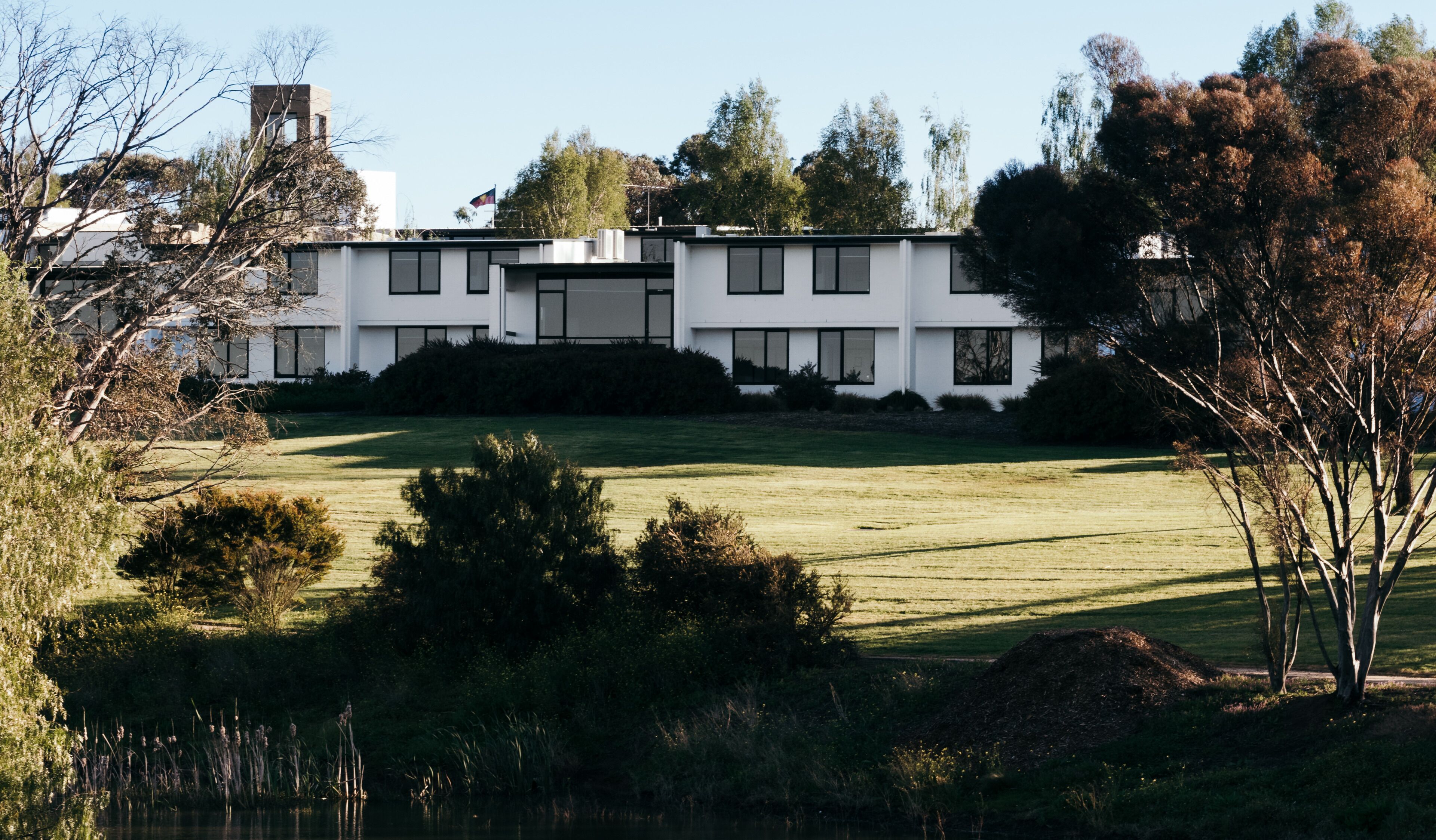 A modern two-story building with a flat roof, surrounded by a well-maintained lawn and trees.