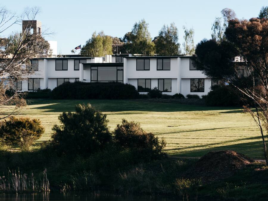 A modern two-story building with a flat roof, surrounded by a well-maintained lawn and trees.