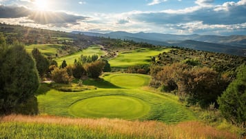 A golf course with multiple green fairways and a scenic mountainous backdrop.