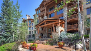 A multi-story hotel with a stone facade, wooden balconies, and a landscaped courtyard with potted plants and a bench. - Beaver Creek Resort (Avon)