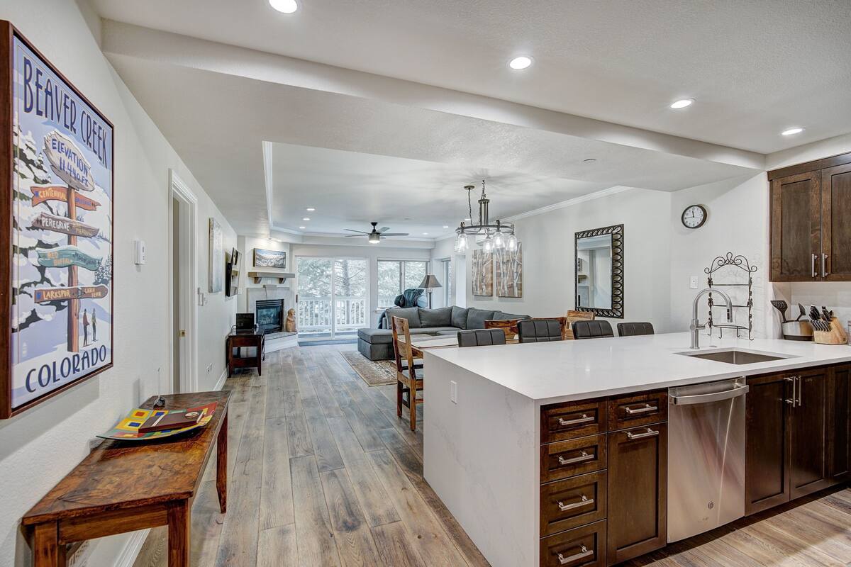 A modern kitchen with a large island, wooden cabinets, and a dining area with a sofa and chairs.