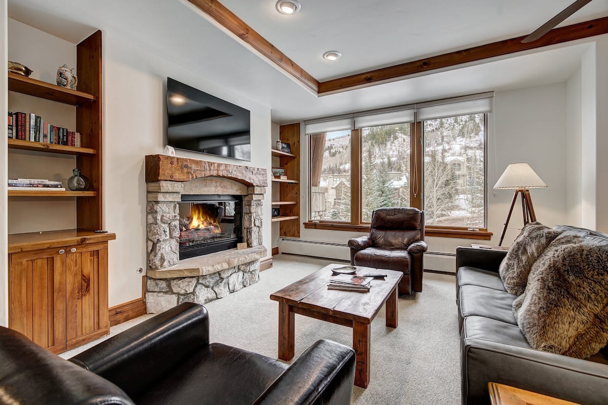 A cozy living room with a stone fireplace, leather sofas, a coffee table, and bookshelves.