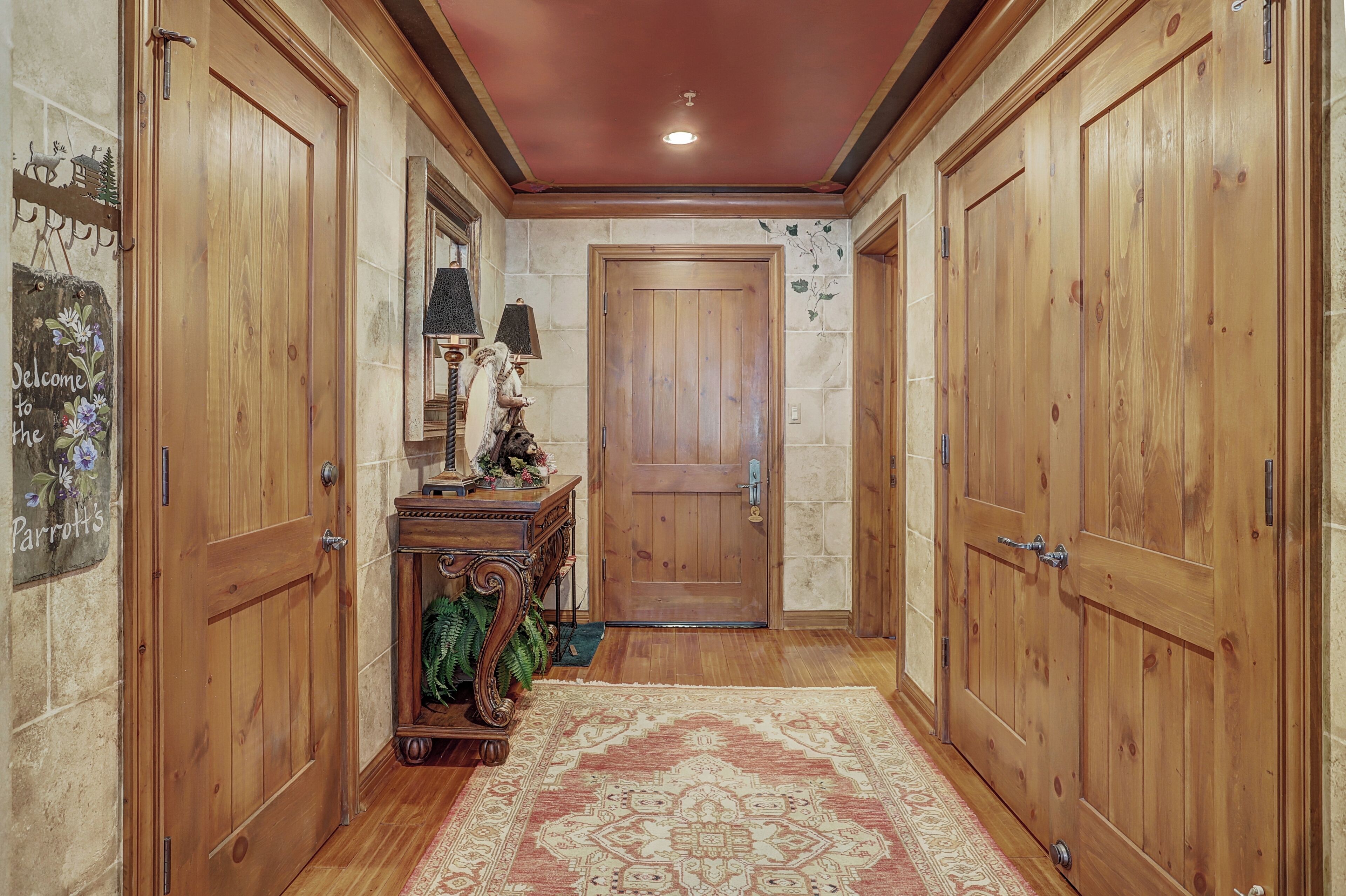 Un pasillo con puertas de madera, una consola de madera con una lámpara y una alfombra estampada.