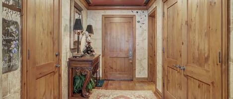 Un pasillo con puertas de madera, una consola de madera con una lámpara y una alfombra estampada.