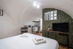 Een compacte kamer met een bed, een televisie, een klein kitchenette en een badkamer.