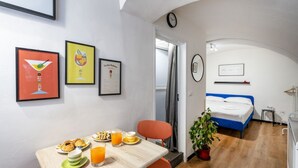 A hotel room with a bed, a dining area with breakfast, a clock, and a plant. - GuestHost - Urban Nest - Comfy Studio in the Heart of Bari (Bari)