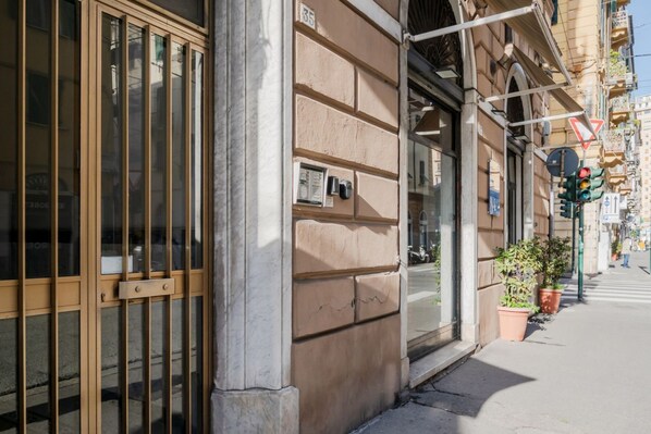 A building facade with large windows, a metal gate, and a street with potted plants.