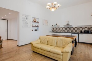 A modern living room with a sofa, a dining table, a kitchen with white cabinets, and a patterned backsplash.