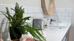 Un baño con un cuenco de madera lleno de caracoles y un helecho, un espejo y un lavabo.