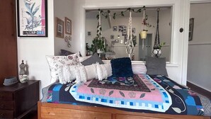 Un dormitorio con una cama de madera, una planta colgante y un cuadro en la pared.