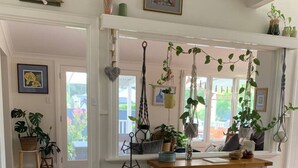 Una habitación con piso de madera, un elegante tocador blanco con cajones, plantas colgantes y vistas al exterior a través de amplios ventanales.
