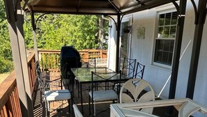 Eine überdachte Terrasse mit Tisch und Stühlen, einem Grill und einem Holzdeck.