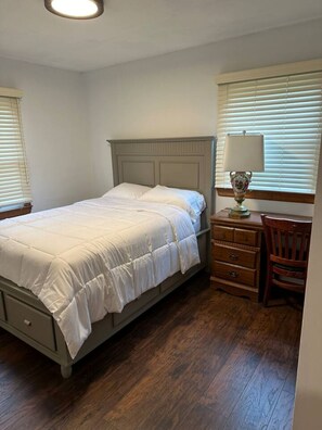 Une chambre à coucher avec un lit, une commode, une chaise et une lampe.