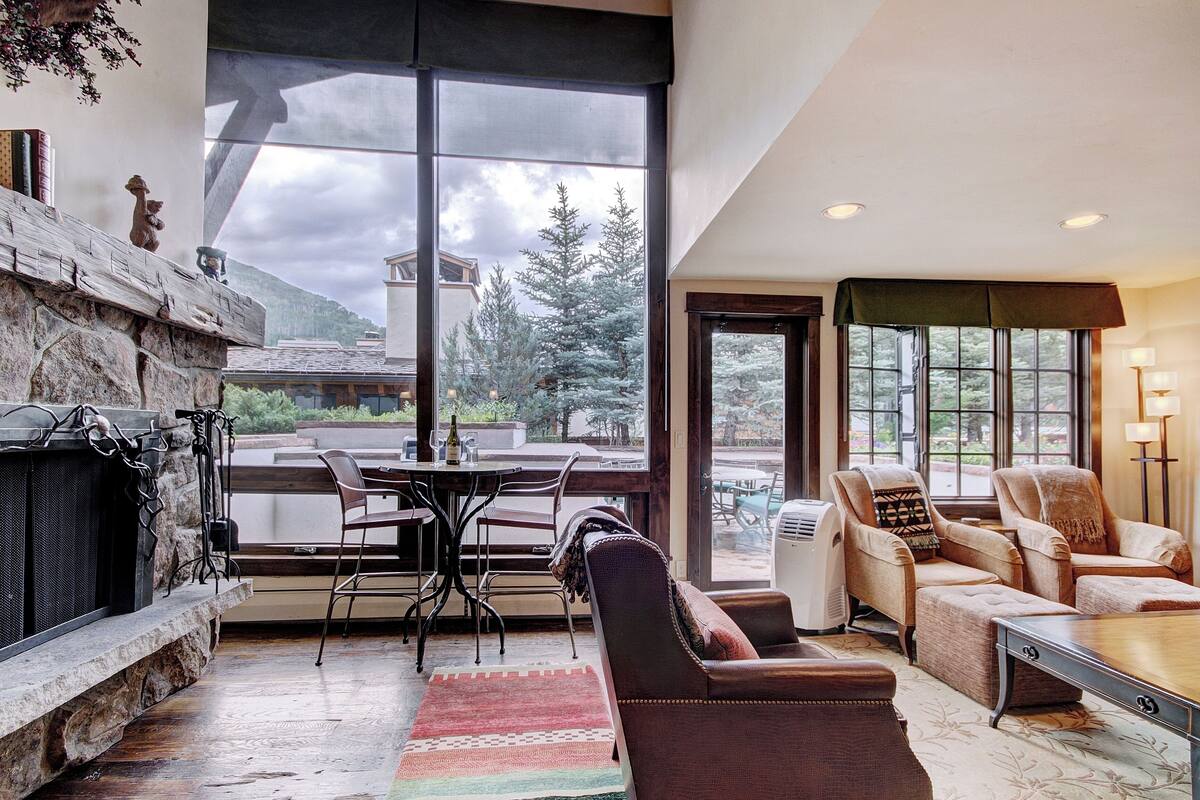 A spacious living room with a fireplace, comfortable seating, and large windows offering a view of the outdoors.