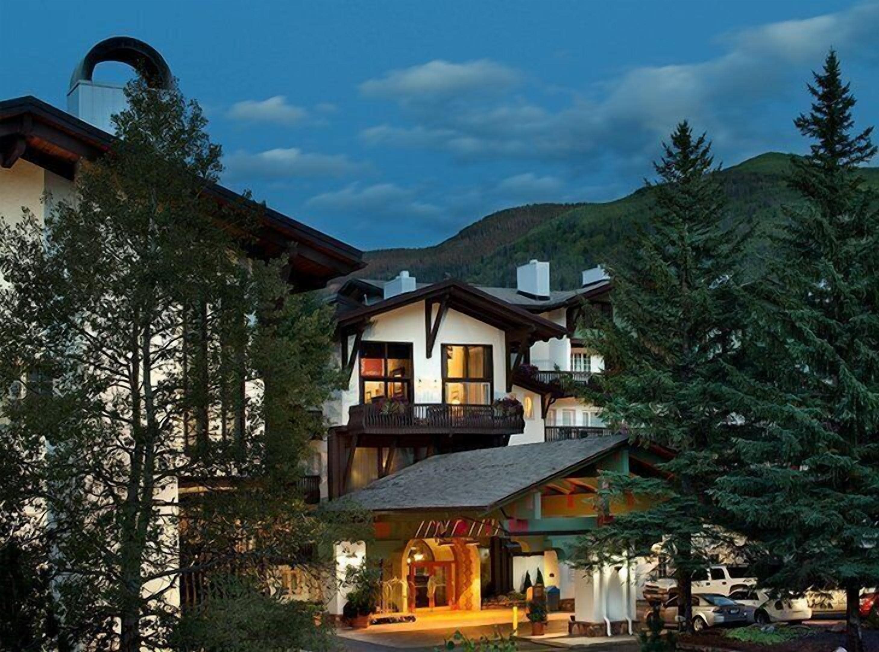 Ein mehrstöckiges Chalet mit Balkon, umgeben von Bäumen und einem Bergpanorama.