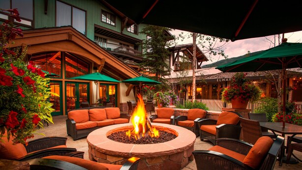 Un patio al aire libre con un hogar de piedra rodeado de muebles de mimbre y sombrillas verdes.