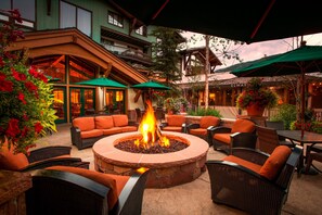 An outdoor patio with a stone fire pit surrounded by wicker furniture and green umbrellas. - Vail Ski Resort (Vail)