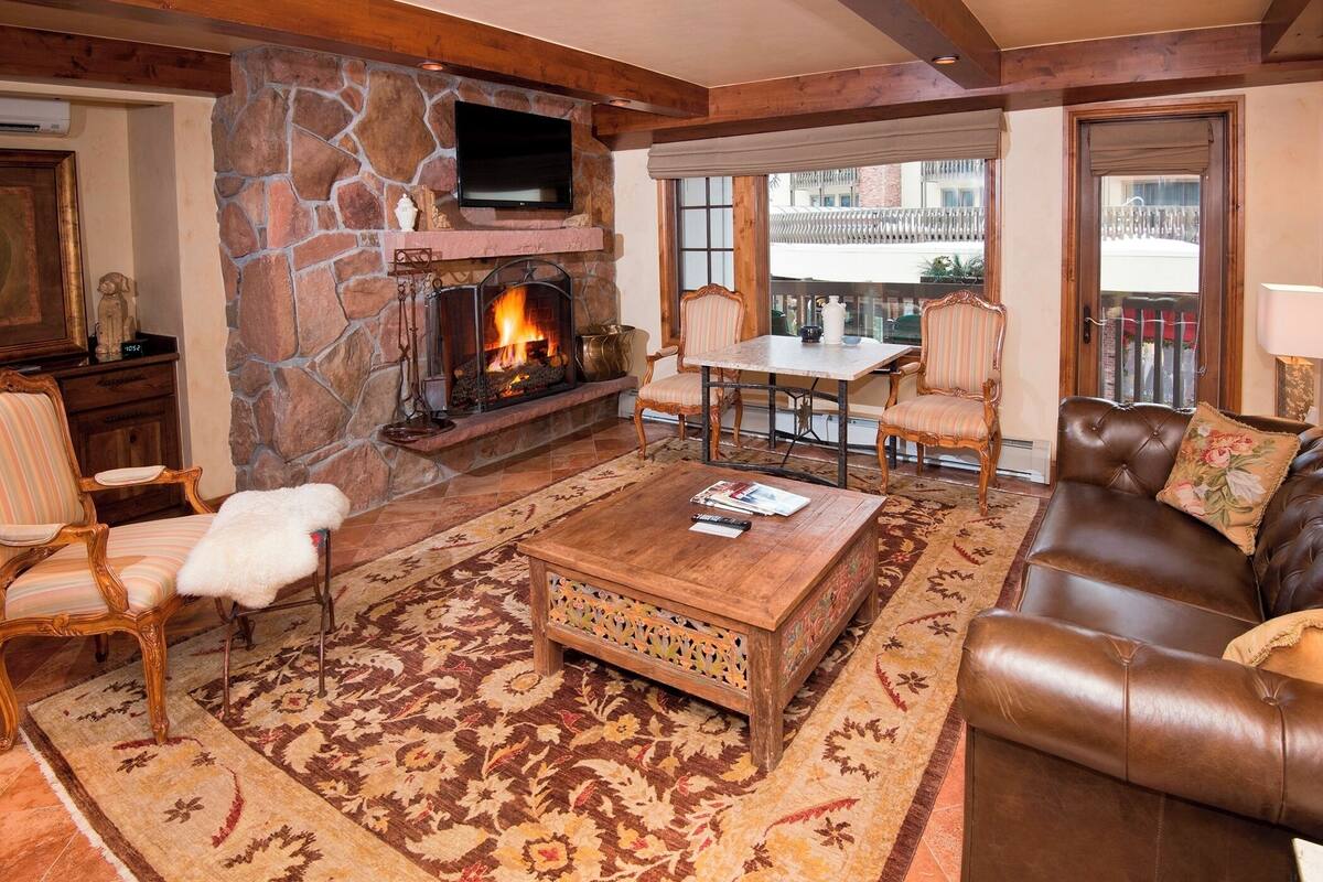 A cozy living room with a stone fireplace, leather sofa, and a television mounted on the wall.
