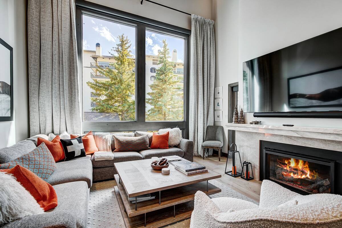 A modern living room with a large window, a fireplace, and a flat-screen TV.