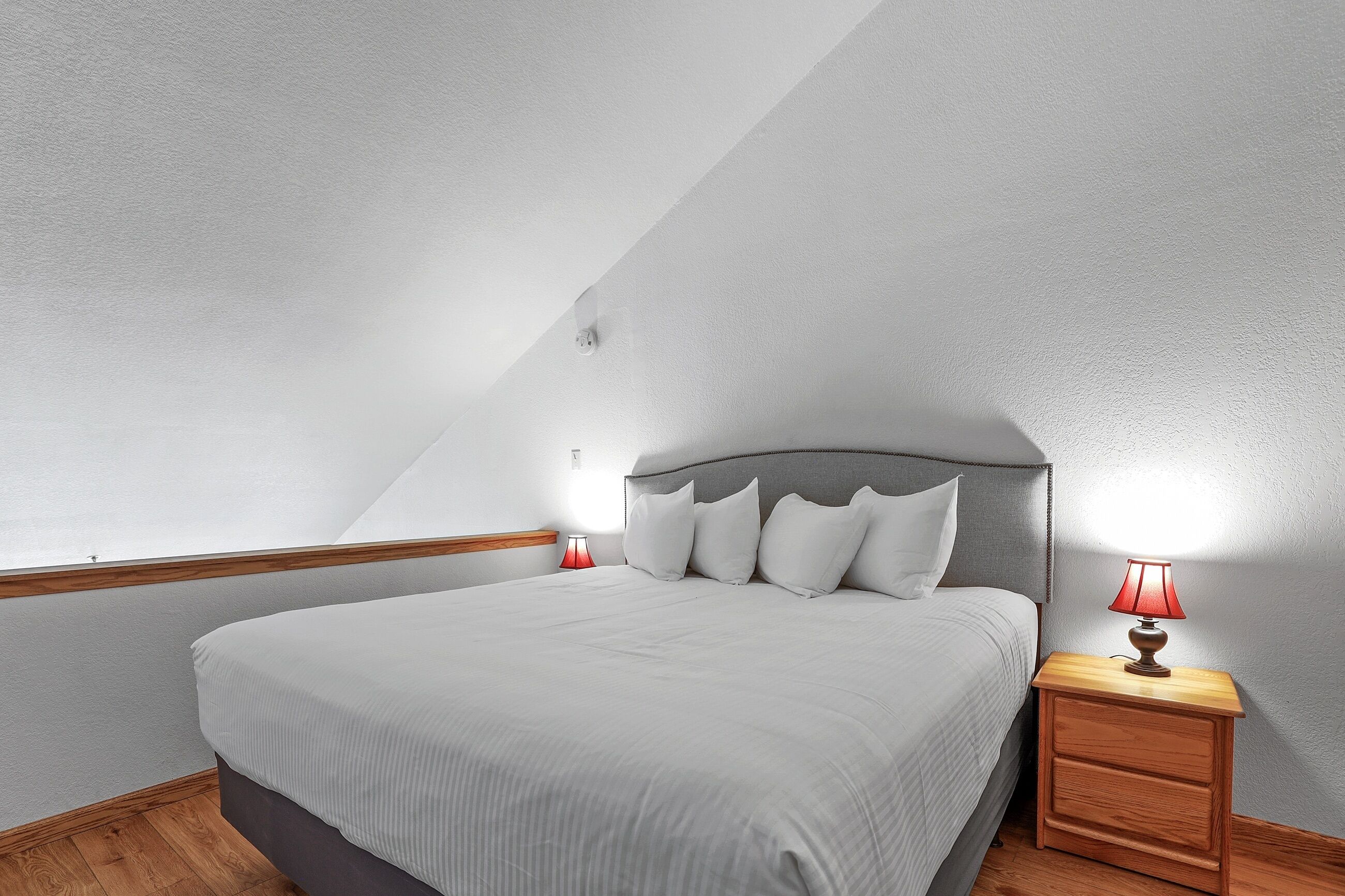 Un dormitorio con cama, mesita de noche y lámpara, y una ventana.