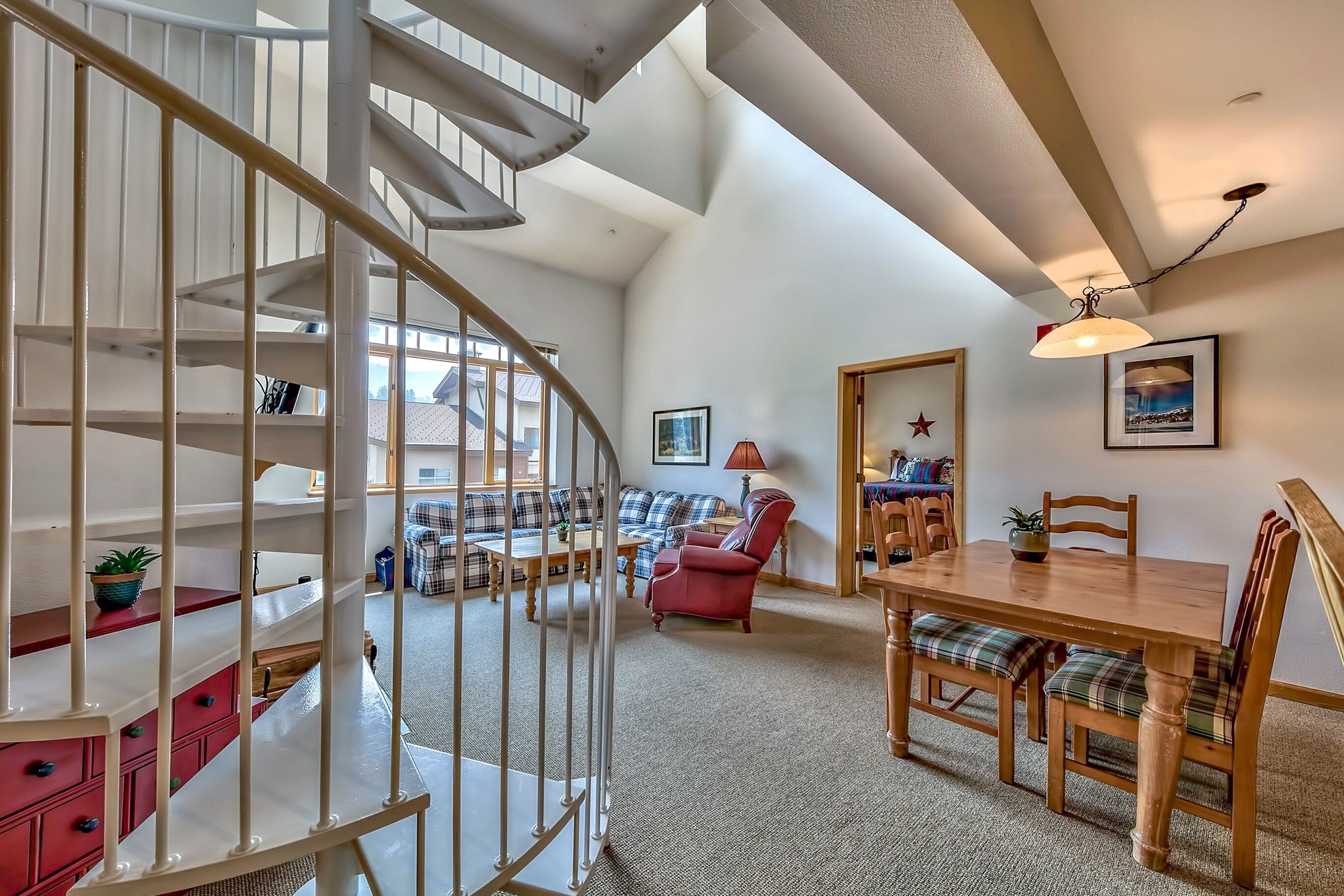 A spacious living area with a spiral staircase, a dining table with chairs, a red armchair, and a sofa set.